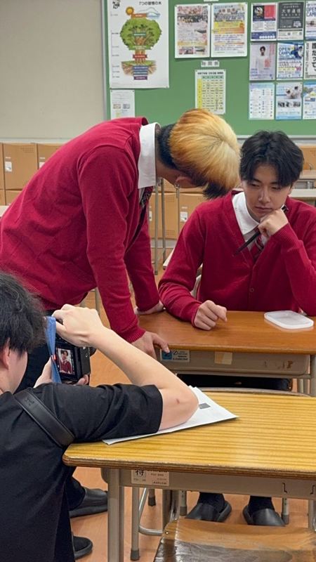 教室で赤いカーディガン姿の出演者を撮影する様子